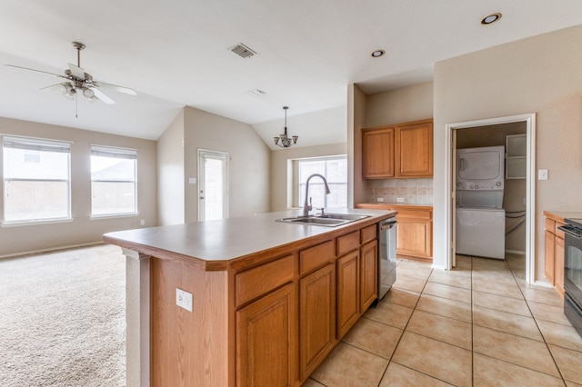 kitchen with ceiling fan with notable chandelier, stacked washer / drying machine, a wealth of natural light, a center island with sink, and sink