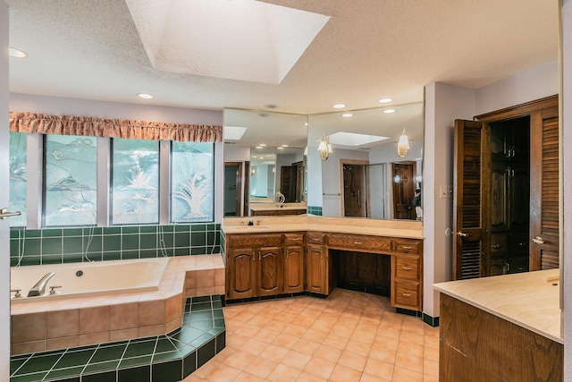 bathroom featuring a skylight, tile patterned flooring, vanity, a relaxing tiled tub, and a textured ceiling