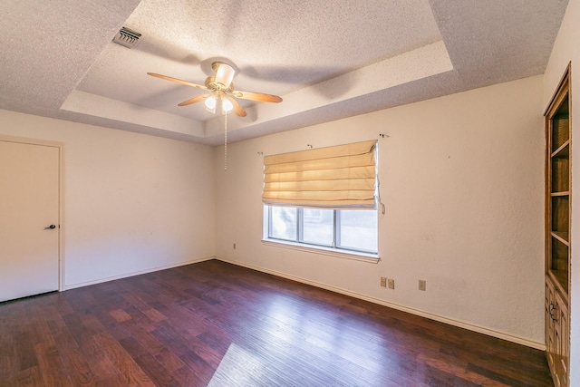 spare room with dark wood-type flooring, a textured ceiling, ceiling fan, and a tray ceiling