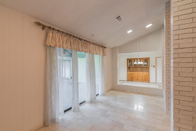 empty room featuring brick wall, lofted ceiling, light tile patterned floors, a textured ceiling, and an inviting chandelier