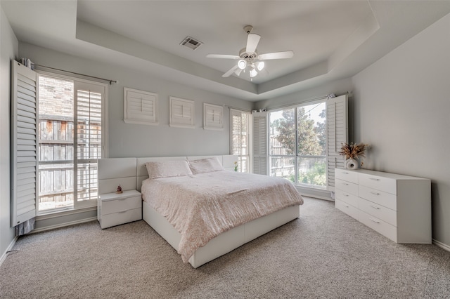 carpeted bedroom with multiple windows, a tray ceiling, and ceiling fan