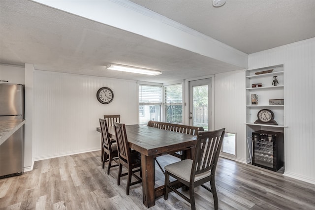 dining area featuring built in shelves, ornamental molding, a textured ceiling, wooden walls, and light hardwood / wood-style floors