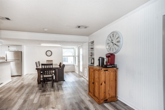 dining area with built in shelves, a textured ceiling, light wood-type flooring, and crown molding