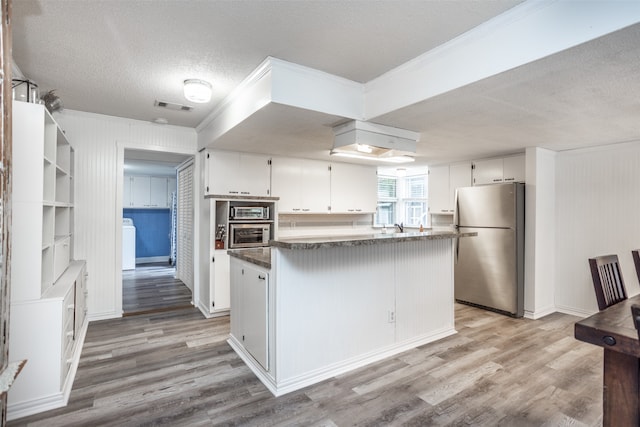 kitchen featuring light hardwood / wood-style flooring, appliances with stainless steel finishes, dark stone counters, and white cabinetry