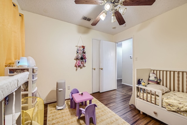 bedroom with a textured ceiling, ceiling fan, a nursery area, and hardwood / wood-style flooring