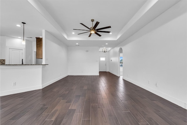 unfurnished living room featuring a raised ceiling, dark wood-type flooring, and ceiling fan