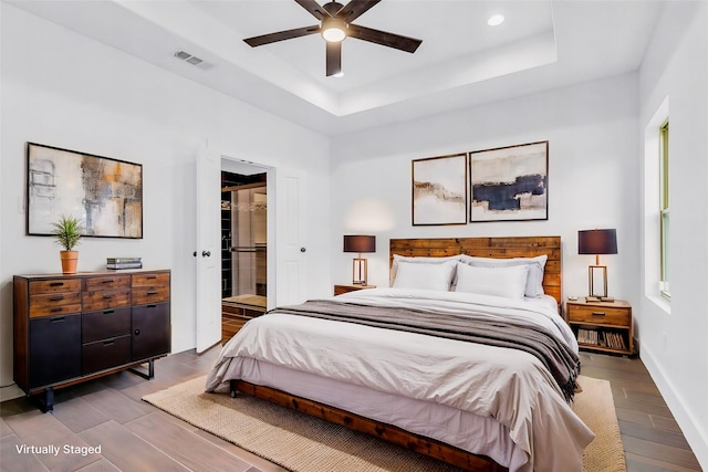 bedroom featuring hardwood / wood-style floors, a walk in closet, ceiling fan, a tray ceiling, and a closet