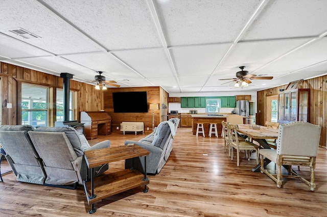 living room featuring ceiling fan, wood walls, light hardwood / wood-style floors, and a wood stove