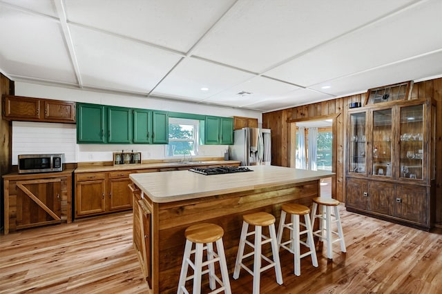 kitchen featuring a center island, wood walls, appliances with stainless steel finishes, light hardwood / wood-style floors, and a breakfast bar area