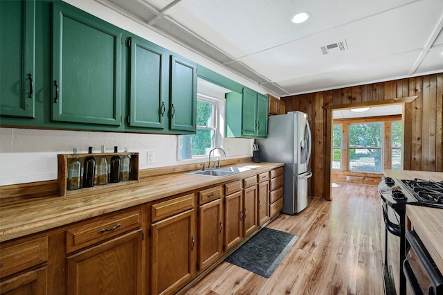 kitchen featuring wooden walls, sink, light hardwood / wood-style flooring, and appliances with stainless steel finishes