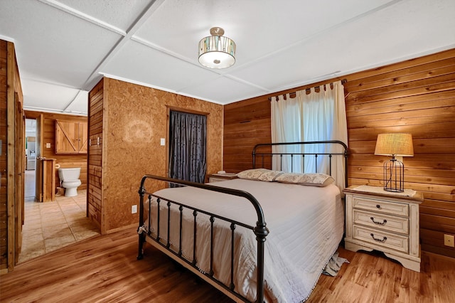 bedroom featuring ensuite bath, wood walls, and light wood-type flooring