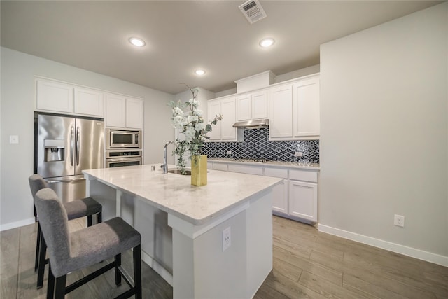 kitchen with a kitchen island with sink, white cabinetry, light hardwood / wood-style flooring, a kitchen breakfast bar, and appliances with stainless steel finishes