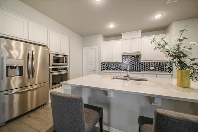 kitchen featuring light stone counters, white cabinets, hardwood / wood-style flooring, appliances with stainless steel finishes, and a breakfast bar