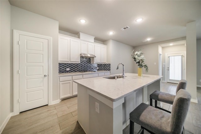 kitchen featuring sink, white cabinetry, light hardwood / wood-style flooring, a center island with sink, and light stone countertops