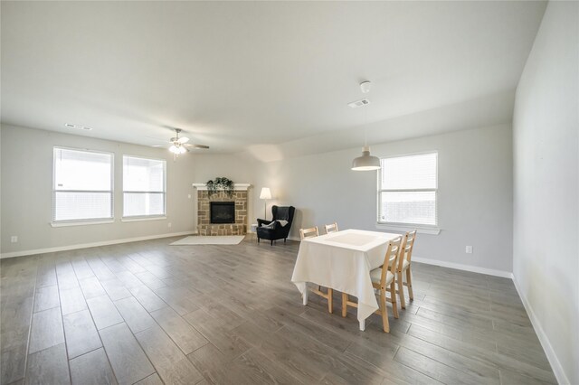 dining space with dark wood-type flooring, a healthy amount of sunlight, and a stone fireplace