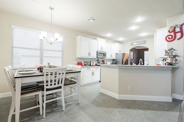 kitchen with a notable chandelier, white cabinets, kitchen peninsula, appliances with stainless steel finishes, and decorative light fixtures