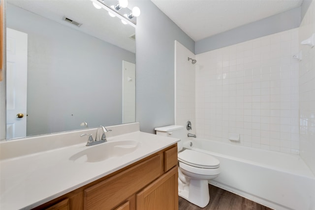 full bathroom with a textured ceiling, hardwood / wood-style floors, tiled shower / bath, vanity, and toilet