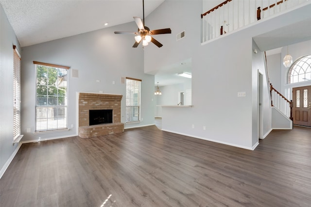 unfurnished living room featuring a brick fireplace, ceiling fan with notable chandelier, and high vaulted ceiling