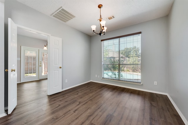 empty room featuring an inviting chandelier, dark wood-type flooring, and a textured ceiling