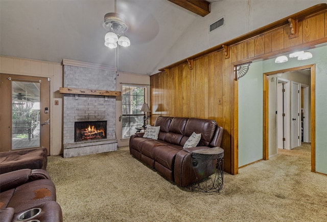 carpeted living room with a brick fireplace, ceiling fan, beamed ceiling, and wooden walls