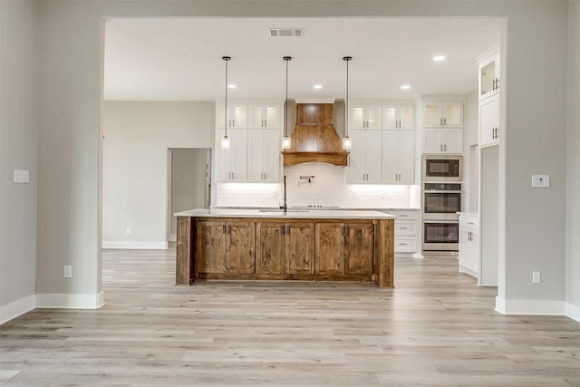 kitchen featuring pendant lighting, white cabinets, a center island with sink, and custom range hood