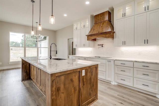 kitchen featuring a center island with sink, white cabinetry, custom exhaust hood, and light stone counters