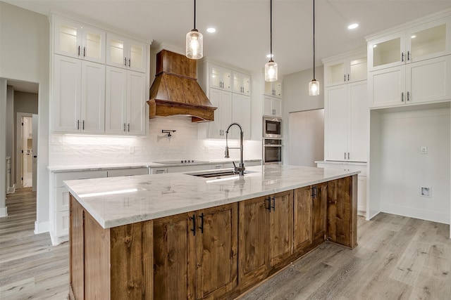 kitchen with custom range hood, a center island with sink, sink, and white cabinets