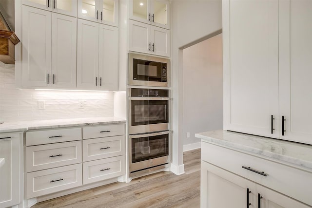 kitchen with decorative backsplash, stainless steel appliances, white cabinetry, and light stone counters