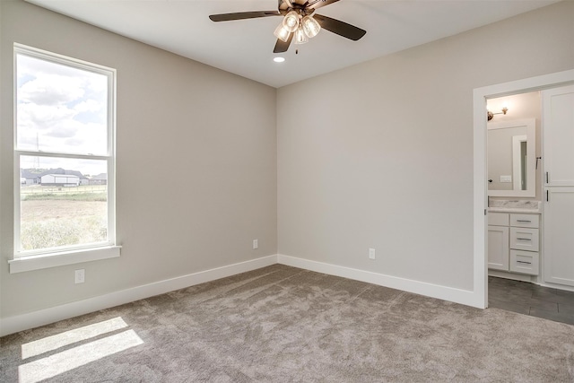 unfurnished bedroom with multiple windows, light colored carpet, ensuite bathroom, and ceiling fan