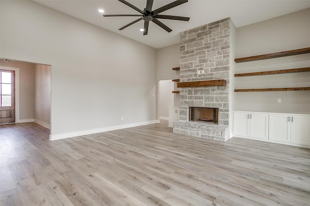 unfurnished living room featuring high vaulted ceiling, a stone fireplace, ceiling fan, and light hardwood / wood-style flooring