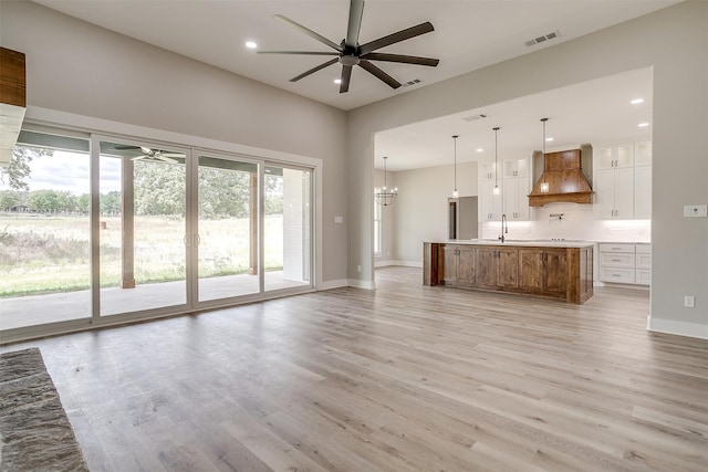 unfurnished living room featuring ceiling fan with notable chandelier, light hardwood / wood-style floors, and sink