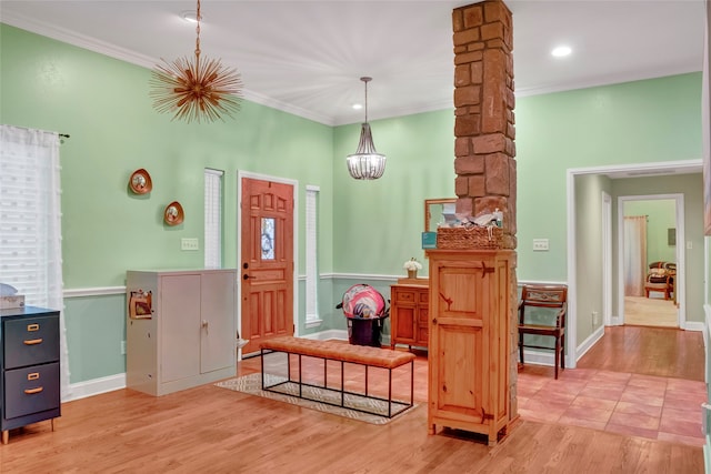 foyer with decorative columns, light hardwood / wood-style floors, ornamental molding, and a notable chandelier