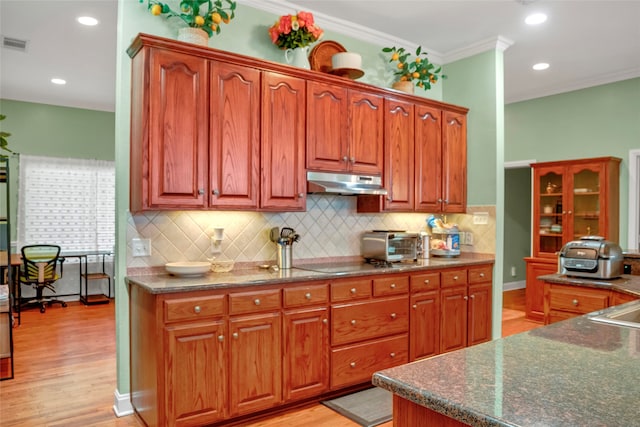 13823 Llano Dr, Weatherford, TX 76087 - kitchen featuring under cabinet range hood, backsplash, light wood finished floors, ornamental molding, and dark stone countertops