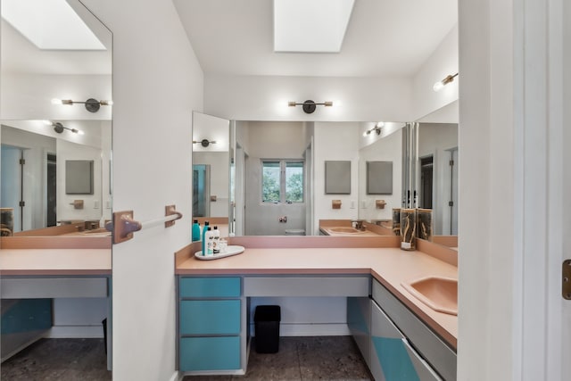 full bath with double vanity, toilet, a skylight, and a sink