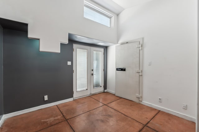 entryway featuring french doors, concrete flooring, baseboards, and a towering ceiling