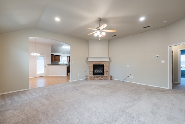 unfurnished living room with a brick fireplace, ceiling fan with notable chandelier, light carpet, and lofted ceiling