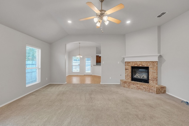 unfurnished living room featuring ceiling fan with notable chandelier, a fireplace, vaulted ceiling, and plenty of natural light