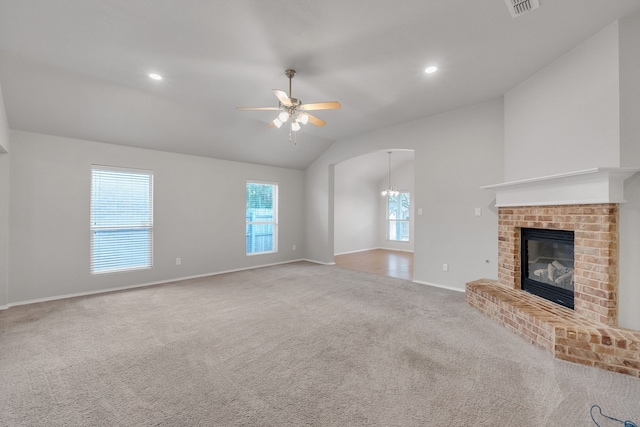 unfurnished living room with ceiling fan with notable chandelier, a brick fireplace, vaulted ceiling, and carpet