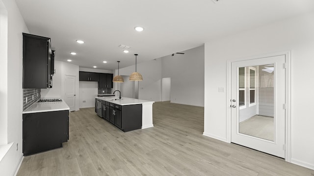 kitchen with decorative light fixtures, a center island with sink, light countertops, a sink, and dark cabinetry