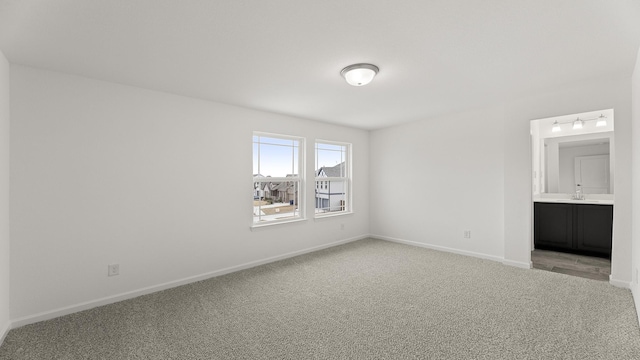 unfurnished bedroom featuring light carpet, connected bathroom, baseboards, and a sink