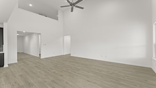 unfurnished living room featuring ceiling fan, a high ceiling, light wood-style flooring, and baseboards