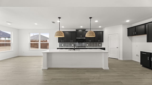 kitchen with dark cabinets, light countertops, hanging light fixtures, and an island with sink