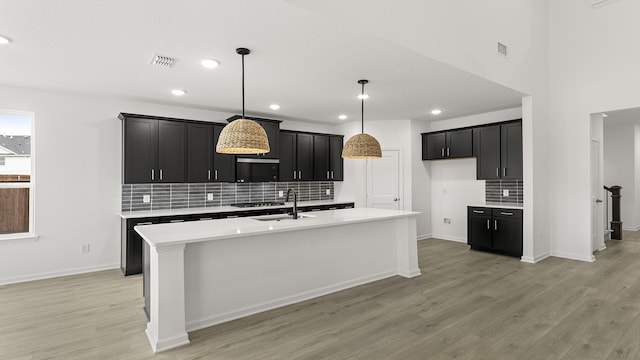 kitchen with a kitchen island with sink, visible vents, light countertops, and dark cabinets