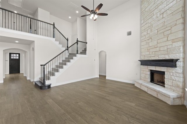 unfurnished living room featuring a towering ceiling, ceiling fan, dark hardwood / wood-style floors, and a stone fireplace