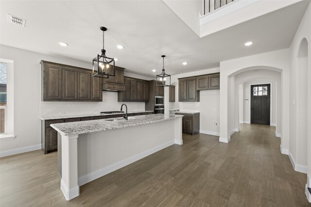 kitchen featuring light stone countertops, a center island with sink, dark wood-type flooring, and a wealth of natural light