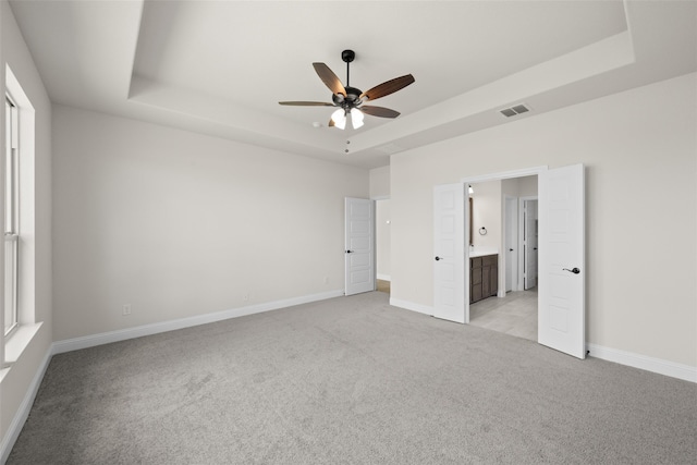 unfurnished bedroom with ceiling fan, a raised ceiling, light carpet, and ensuite bathroom