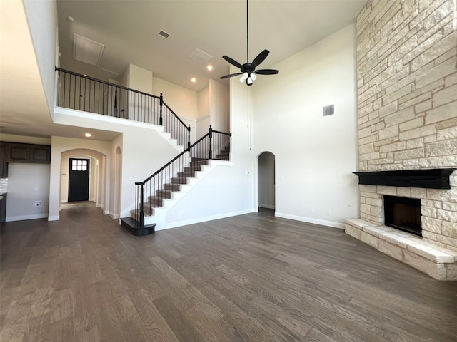 unfurnished living room featuring ceiling fan, a stone fireplace, a towering ceiling, and dark hardwood / wood-style floors