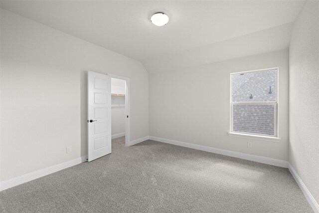 unfurnished bedroom featuring carpet floors, lofted ceiling, a walk in closet, and a closet