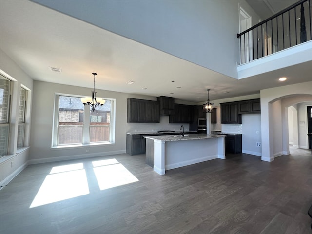 kitchen featuring dark wood-type flooring, light stone counters, a center island with sink, sink, and a chandelier