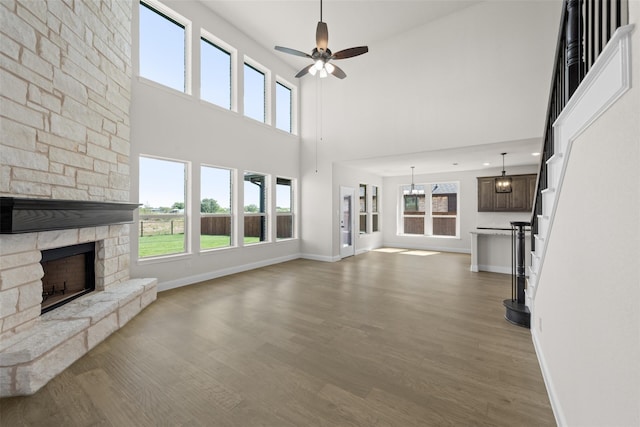 unfurnished living room with ceiling fan, a fireplace, a towering ceiling, and light hardwood / wood-style flooring